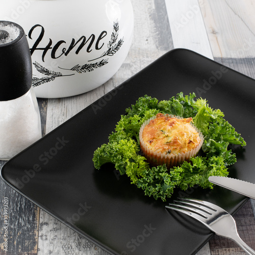 Freshly Baked Courgette and Tuna Muffins on a dark plate with kale. Proposal of serving the dish.