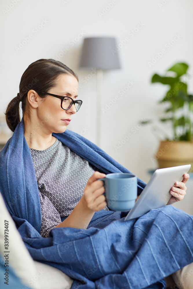 Young woman in eyeglasses resting on sofa with cup of tea and watching something on digital tablet at home Young woman in eyeglasses resting on sofa with cup of tea and watching something on digital tablet at home