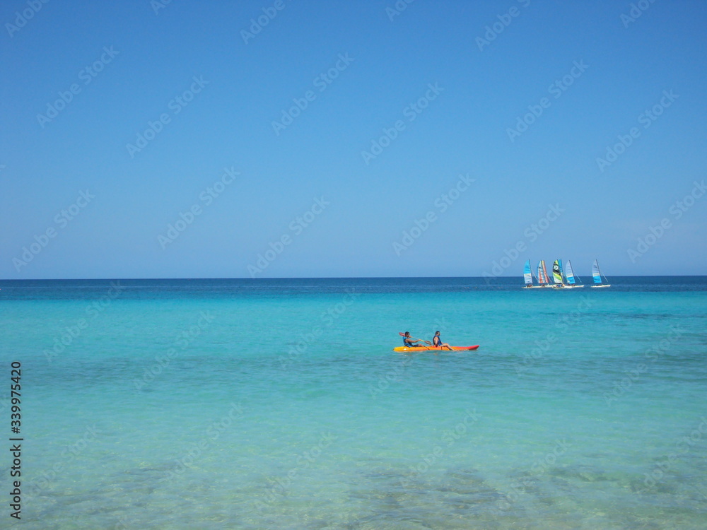 Mar turquesa paradisíaco con dos personas en bote a remo y barcas de vela