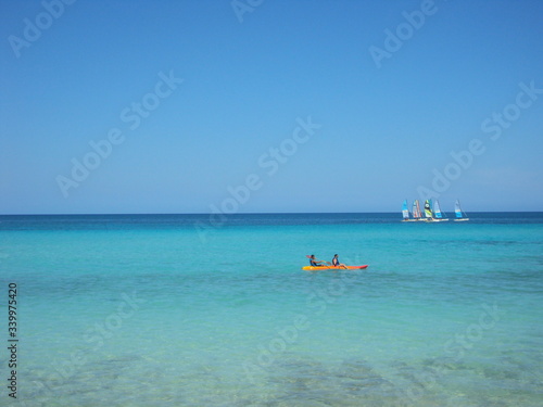 Mar turquesa paradisíaco con dos personas en bote a remo y barcas de vela © Cesar Tezza