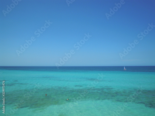 Mar turquesa paradisíaco con dos personas nadando y barca de vela