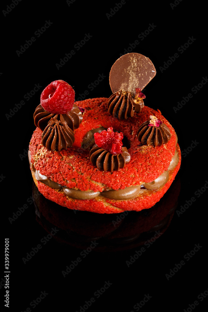 Naklejka premium Choux cream. Red velvet sweet bagel with Carmel cream filling and chocolate icing, raspberry fruit on top. Confectionery photography concept.