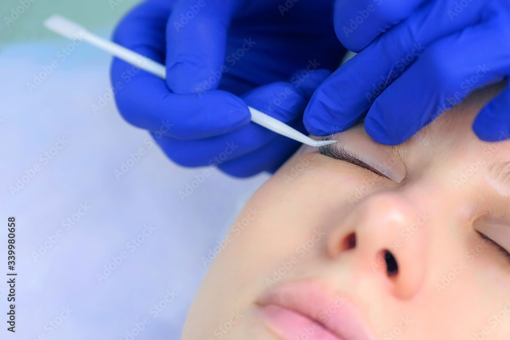 Naklejka premium Cosmetologist bending lashes with needle into curlers, lift eyelashes laminaton procedure in beauty salon for woman, closeup face. Beautician making lash lifting in cosmetology clinic, hands closeup.