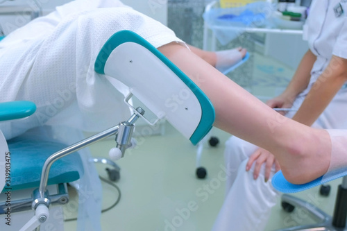 Unrecognizable patient woman in gynecological chair in clinic  side view. Modern interior in medical office. Doctor gynecologist preparing to inspection. Examination and consultation of gynecologist.
