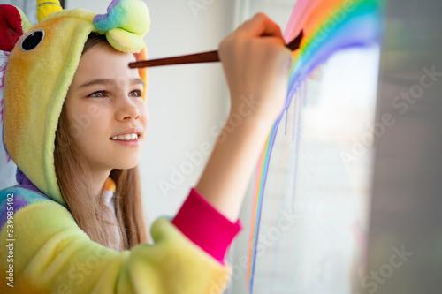 teen in kigurumi draws rainbow on window home photo