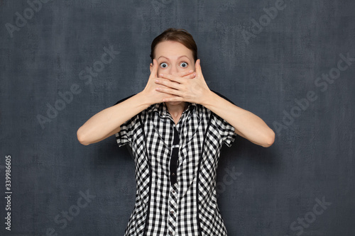 Portrait of shocked young blond woman covering mouth with hands