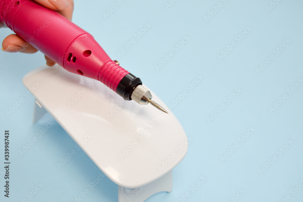 The process of making a beautiful manicure on the hands on the fingers with the help of a special machine and a lamp for drying the varnish in the nail beauty salon on a blue background The process of making a beautiful manicure on the hands on the fingers with the help of a special machine and a lamp for drying the varnish in the nail beauty salon on a blue background