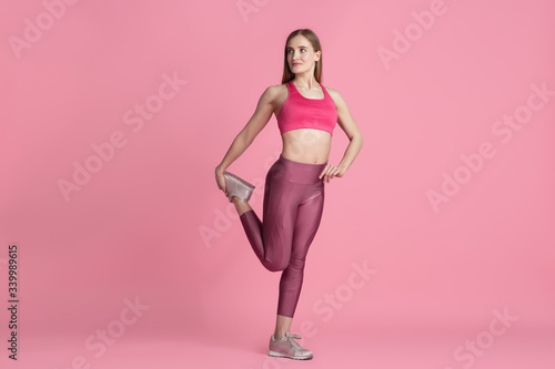 Fototapeta Naklejka Na Ścianę i Meble -  Stretching. Beautiful young female athlete practicing in studio, monochrome pink portrait. Sportive fit caucasian model training. Body building, healthy lifestyle, beauty and action concept.