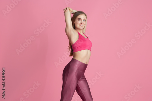 Graceful. Beautiful young female athlete practicing in studio, monochrome pink portrait. Sportive fit caucasian model posing. Body building, healthy lifestyle, beauty and action concept.