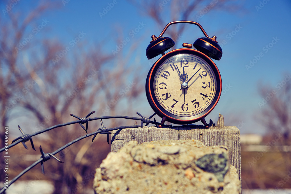 Fototapeta premium Old retro alarm clock on post tied with barbed wire symbolizes arrival of spring.