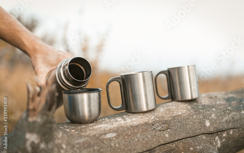 Males Hands Pouring Hot Drink From Thermos In Mugs