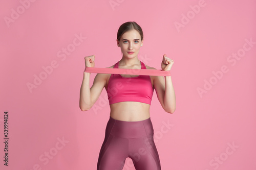 Upper body. Beautiful young female athlete practicing in studio, monochrome pink portrait. Sportive fit caucasian model with elastics. Body building, healthy lifestyle, beauty and action concept. © master1305