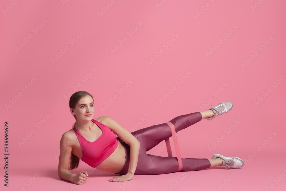 Upper body. Beautiful young female athlete practicing in studio, monochrome pink portrait. Sportive fit caucasian model with elastics. Body building, healthy lifestyle, beauty and action concept. Upper body. Beautiful young female athlete practicing in studio, monochrome pink portrait. Sportive fit caucasian model with elastics. Body building, healthy lifestyle, beauty and action concept.