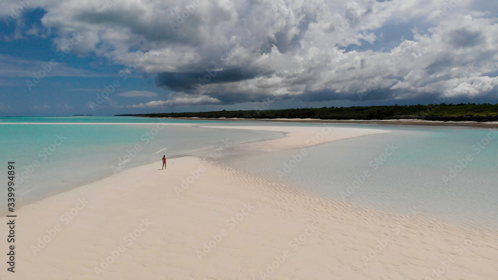 Aerial drone view of a woman walking alone trough a sandbank near to the clear blue water of Indian Ocean 