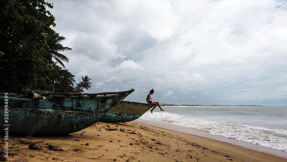 Brunette woman sit on traditional wooden fishing boats in a tropical beach of Sri Lanka