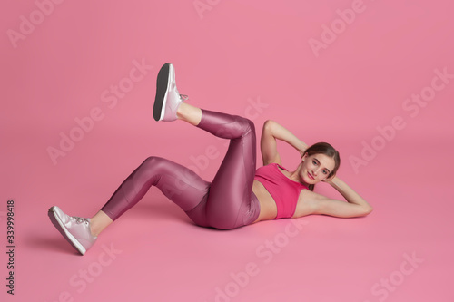 ABS' crunches. Beautiful young female athlete practicing in studio, monochrome pink portrait. Sportive fit caucasian model training. Body building, healthy lifestyle, beauty and action concept.