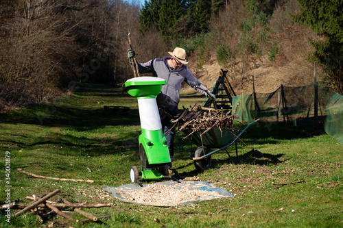 Gardener using electric shredder or wood chipper for shredding tree or shrub cuttings. photo