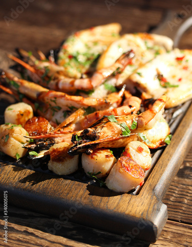Fried prawns shrimps, squid and scallops with herbs, pepper and spices on wooden board.  Summer picnic, sunny day. Background image, copy space