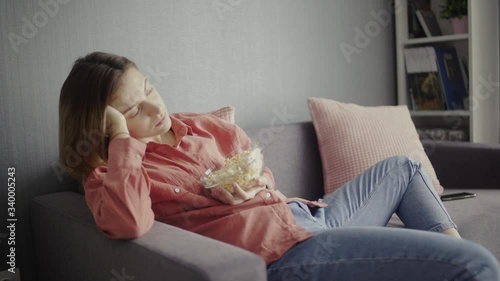Young woman sitting on the sofa, eating popcorn, watching TV and falling alseep photo