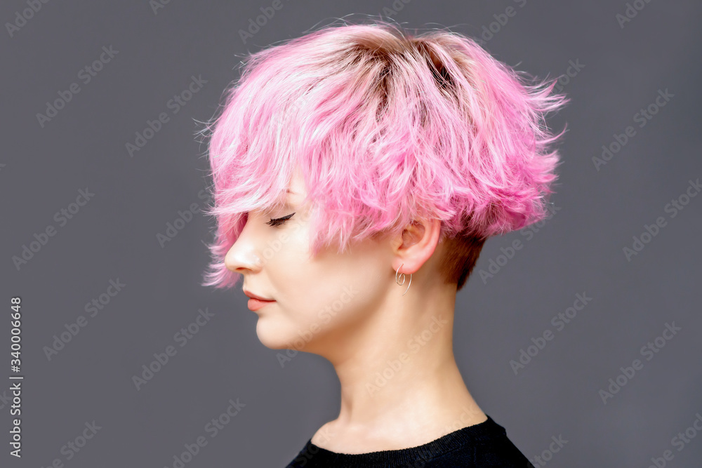 Woman with pink hairstyle standing on gray background, side view.