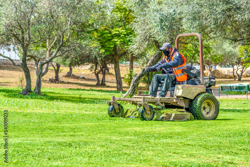 Man wear safety masks as a precaution after outbreak the Covid 2019 during mows the grass with lawn mower.