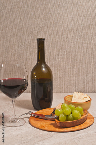 Top, front view, medium distance of a glass ofwhite wine, bottle of wine, corkscrew, artisan bowl of cheese, on rare wood plate photo