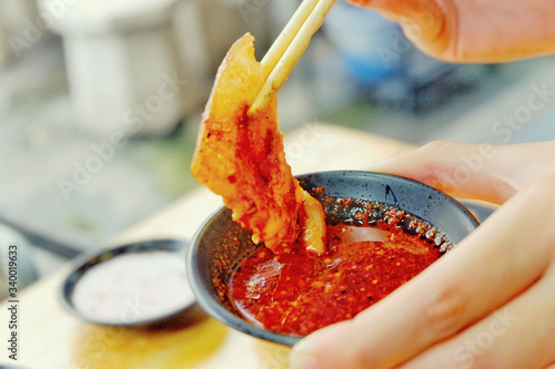 The hand is used to hold the chopsticks to bring the grilled pork to dip in tasty sauce. Sliced pork grill with sauce in barbecue shop.Close up.