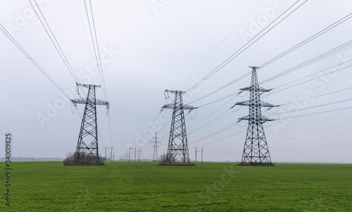 Electrical net of poles on a panorama of blue sky and green meadow