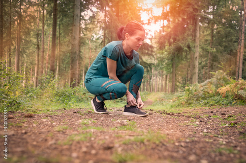 Sporty woman tying up her shoelace before exercise, woodland setting.