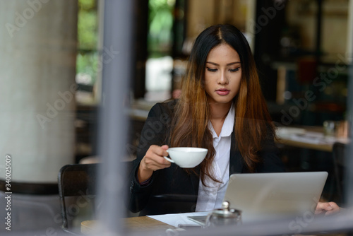Young Asian businesswoman drinking coffee while working at cafe