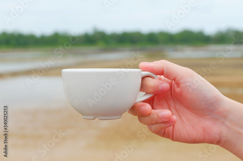 Canvas Print Hand women hodling white coffee cup with salt farm background