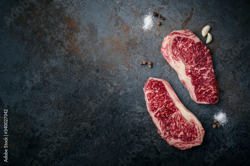 Two raw, fresh Wagyu marbled beef steaks, strip loin on a dark stone background, top view and copy space photo