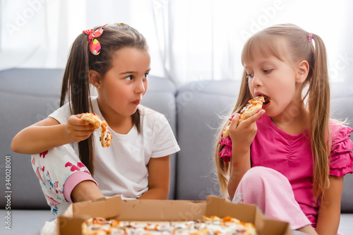 Two little girls eating huge pizza at home