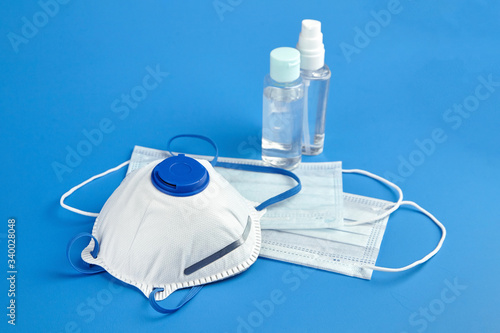 Respirator n95, FFP2, bottles of antibacterial hand sanitizer (alcohol antiseptic gel) and surgical masks on blue background