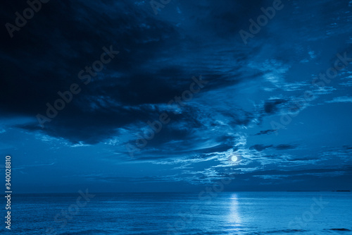 This photo illustration of a deep blue moonlit ocean and sky at night  would make a great travel background for any travel or vacation purpose. © ricardoreitmeyer