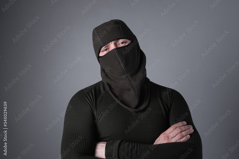 A man in a balaclava, as a special forces concept, stands with a menacing look, clasped hands on his chest A man in a balaclava, as a special forces concept, stands with a menacing look, clasped hands on his chest