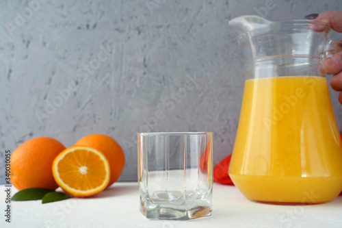 Empty glass and hand of woman holding decanter with orange juice. Oranges on the table