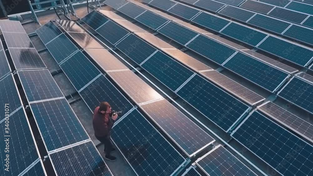 Solar energy farm on roof. Male photographer doing photos among the blue solar panels at sunset. Clean alternative energy from the evening sun. View from above. Solar energy farm on roof. Male photographer doing photos among the blue solar panels at sunset. Clean alternative energy from the evening sun. View from above.