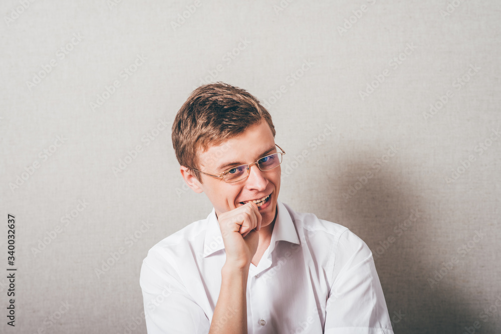 The man with glasses biting his fists, bites his nails. On a gray background. The man with glasses biting his fists, bites his nails. On a gray background.