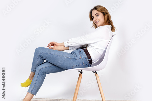 young girl in a white shirt and jeans sits on a chair on a white background