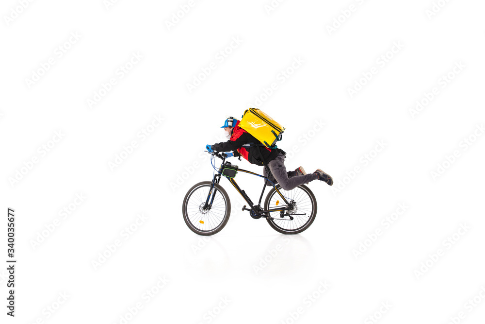 Fototapeta premium Too much orders. Contacless delivery service during quarantine. Man delivers food during isolation, wearing gloves and face mask. Taking pizza on bike isolated on white background. Safety. Hurrying up