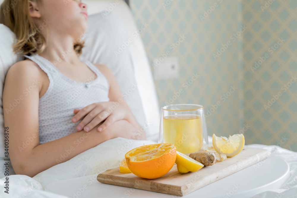 Little sick girl in bed with cup of antipyretic drugs for colds,flu.Tea with citrus vitamin C,ginger root,lemon,orange.Wooden tray. Home self-treatment.Medical quarantine covid-19 coronavirus therapy Little sick girl in bed with cup of antipyretic drugs for colds,flu.Tea with citrus vitamin C,ginger root,lemon,orange.Wooden tray. Home self-treatment.Medical quarantine covid-19 coronavirus therapy