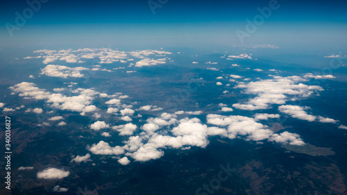 Aerial view of mountains under the clouds and blue sky. View from a plane window. Beautiful landscape