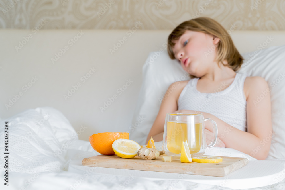 Little sick girl in bed with cup of antipyretic drugs for colds,flu.Tea with citrus vitamin C,ginger root,lemon,orange.Wooden tray. Home self-treatment.Medical quarantine covid-19 coronavirus therapy Little sick girl in bed with cup of antipyretic drugs for colds,flu.Tea with citrus vitamin C,ginger root,lemon,orange.Wooden tray. Home self-treatment.Medical quarantine covid-19 coronavirus therapy