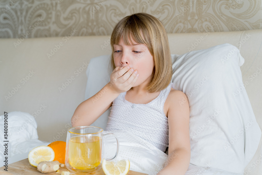 :ittle sick girl in bed coughs in hand. Cup of tea with citrus vitamin C,ginger root,lemon,orange. Drugs for colds,flu.Wooden tray.Home self-treatment.Medical quarantine.Covid-19,coronavirus therapy :ittle sick girl in bed coughs in hand. Cup of tea with citrus vitamin C,ginger root,lemon,orange. Drugs for colds,flu.Wooden tray.Home self-treatment.Medical quarantine.Covid-19,coronavirus therapy