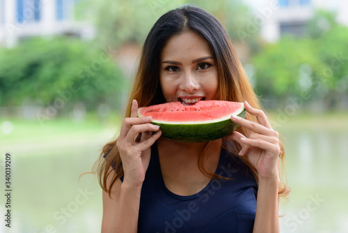 Happy young beautiful Asian woman eating watermelon at the park