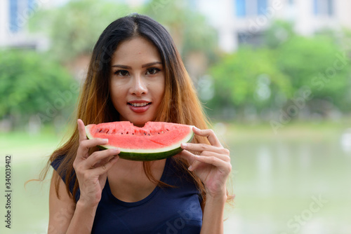Happy young beautiful Asian woman eating watermelon at the park