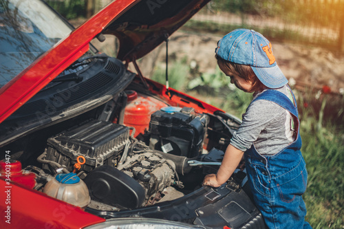Little child trying to fix broken real car. Dreaming to be auto technician