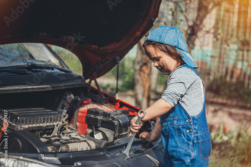 Little child trying to fix broken real car. Dreaming to be auto technician