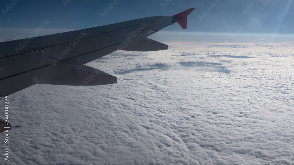Fototapeta premium Wing of airplane flying above clouds in the sky and with a view thick clouds under sunny rays.